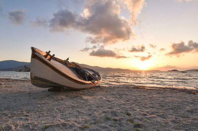 Boat moored on beach against sky during sunset