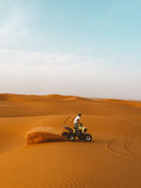 Man riding motorcycle on sand in desert against sky