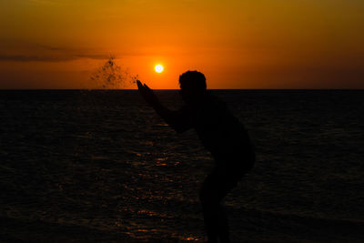 Silhouette person by sea against sky during sunset