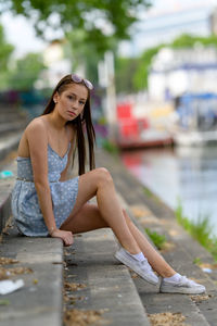 A portrait of a pretty young woman taken in the summertime in a city sitting on a staircase.