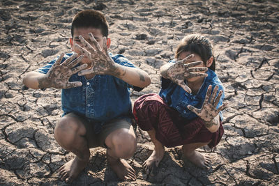 Siblings with messy hands gesturing while crouching on ground