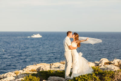 Couple kissing on shore against sea