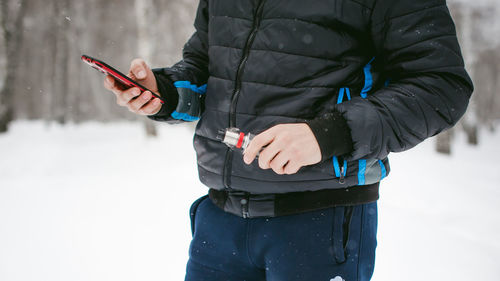 Midsection of man using mobile phone while standing on snow