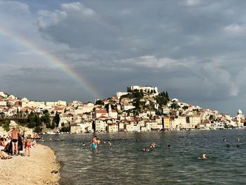 Buildings by sea against rainbow in sky