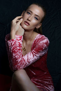 Close-up portrait of beautiful woman with blue eyes sitting against wall