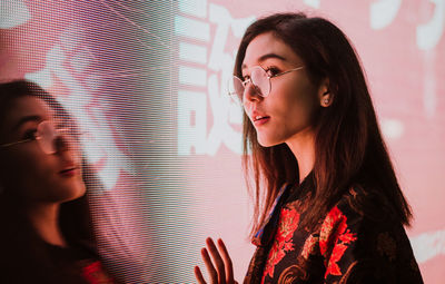 Close-up of young woman standing against illuminated city at night