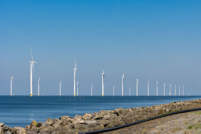 Wind turbines by sea against clear blue sky,