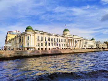 View of building by river against cloudy sky