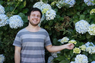 Portrait of smiling man standing by hydrangea flowers at park