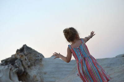 Woman on rock at beach against clear sky