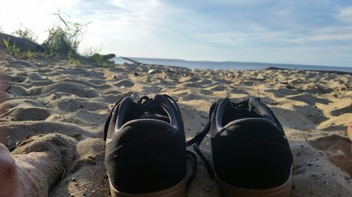 Low section of person with shoes at beach against sky