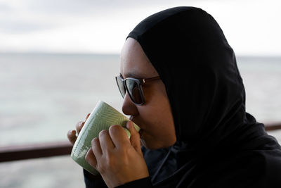 Close-up of woman wearing hijab drinking coffee against sea