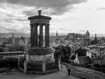 Monument and buildings in city against cloudy sky