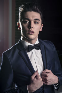 Portrait of young man standing against black background