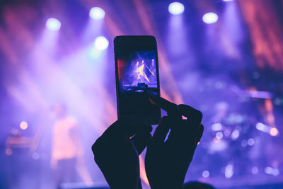 Cropped hand photographing music concert at night