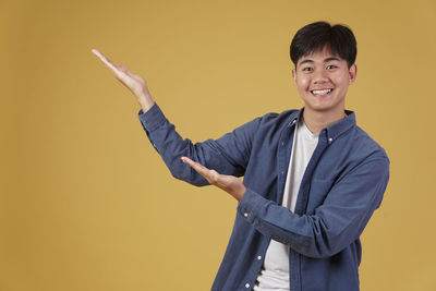 Portrait of young man standing against yellow background