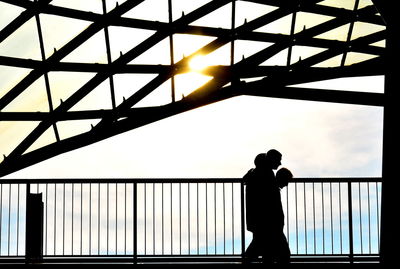 Silhouette man standing by railing against sky during sunset