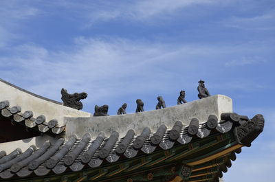 Low angle view of statues on building roof against sky