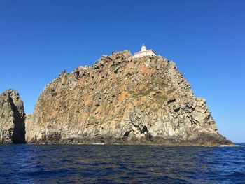 Rock formations in sea against clear blue sky