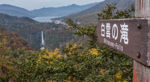 Close-up of signboard by waterfall amidst tree and mountain 