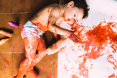 High angle view of child lying with paint on floor at home