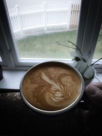 Close-up of hand holding cappuccino served on table