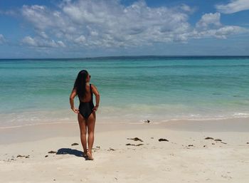 Full length of shirtless woman standing on beach against sky