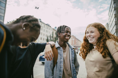 Happy braided hair teenage boy enjoying with friends under cloudy sky