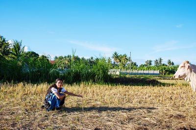 Woman with cow crouching on agricultural field