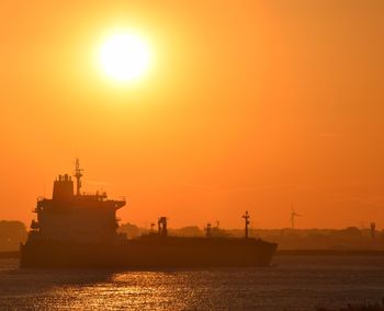 Ship sailing in sea against orange sky