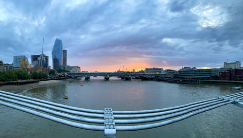 Bridge over river in city against sky during sunset