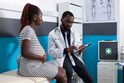 Smiling doctor using digital tablet while talking with pregnant woman in clinic