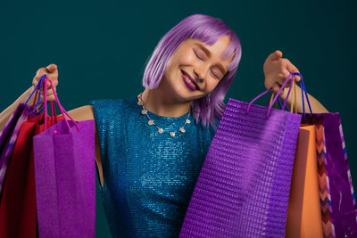 Smiling young woman holding shopping bags against colored background