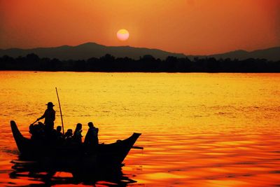 Silhouette people in sea against orange sky