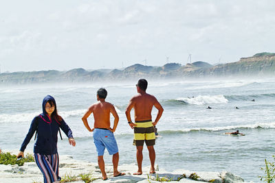 Rear view of men standing at beach against sky