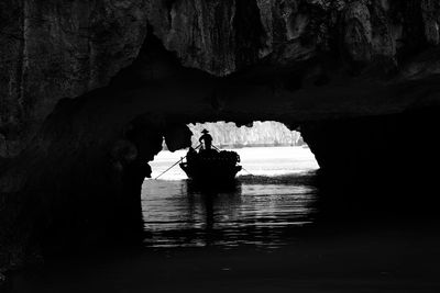 Silhouette person in boat and cave on sea