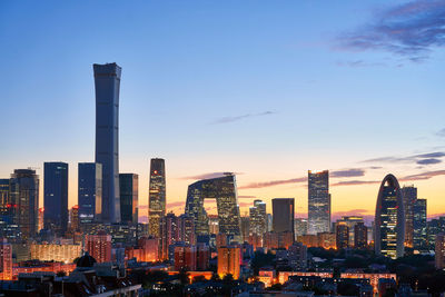 Illuminated buildings in city against sky during sunset