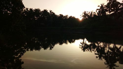 Silhouette trees by lake against sky during sunset