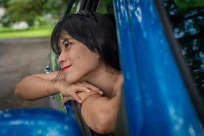 Portrait of young woman looking away while sitting on car