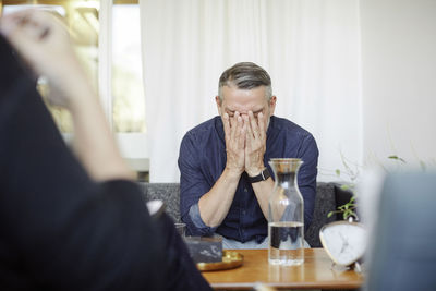 Stressed male patient covering face while sitting with doctor at community center