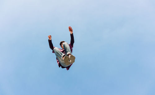 From below of male jumping above ground and performing parkour stunt on background of blue cloudless sky