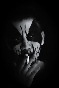 Close-up of man with zombie face paint smoking cigarette against black background