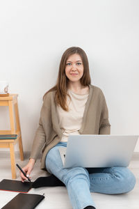 Woman graphic designer sitting on floor and working on a laptop. girl using digital tablet in work