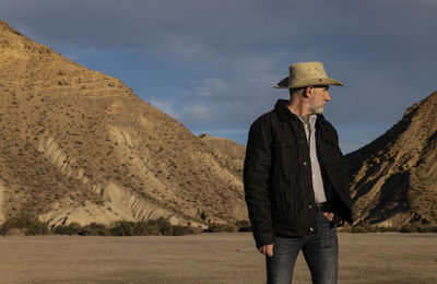 Adult man in cowboy hat standing against mountains in tabernas desert. almeria, spain