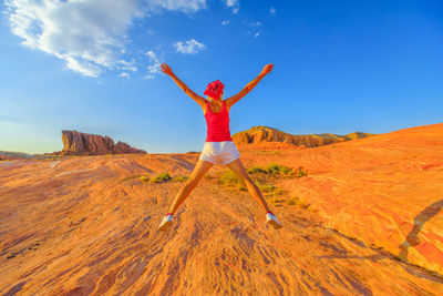 Woman jumping with arms outstretched against sky