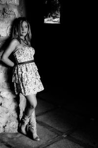 Black and white portrait of young woman leaning against wall at the entrance of a tunnel
