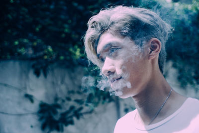 Close-up of young man looking away while emitting smoke