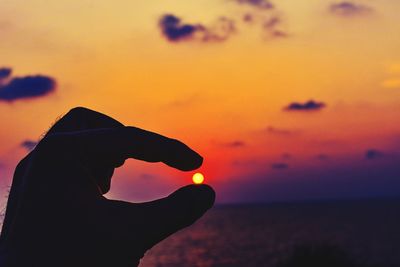 Silhouette hand holding orange sky during sunset