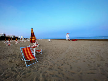 Deck chairs on beach against clear blue sky