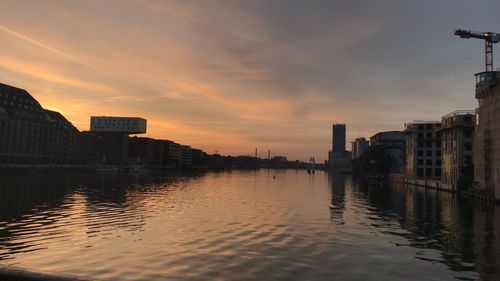 Buildings by river against sky during sunset